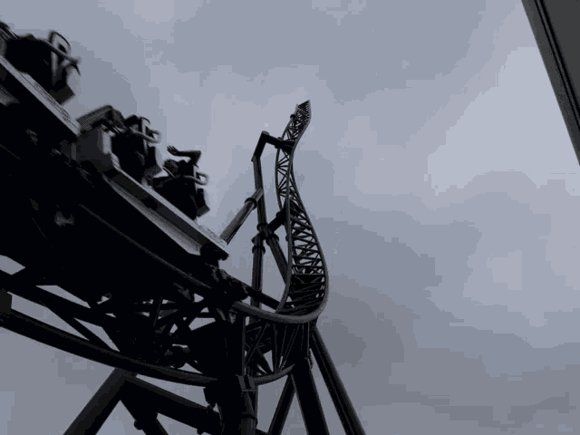 a roller coaster going up a hill with a cloudy sky behind it
