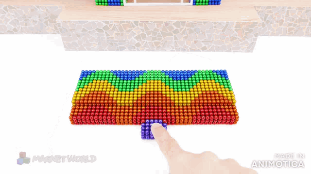 a person is playing with a rainbow colored mat made of magnet beads