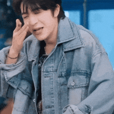 a man wearing a denim jacket is making a face