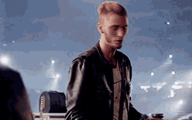 a man in a leather jacket is standing in front of a stage holding a green bottle .