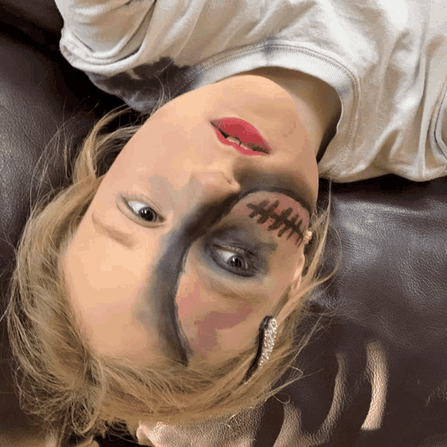 a girl with stitches painted on her face laying on her back