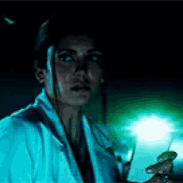 a woman in a white coat is holding a cell phone in her hand in the dark .