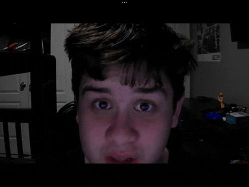 a man 's face is shown in a dark room with a picture of a city on the wall behind him