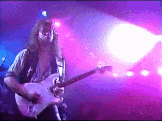 a man with long hair is playing a guitar in a dark room
