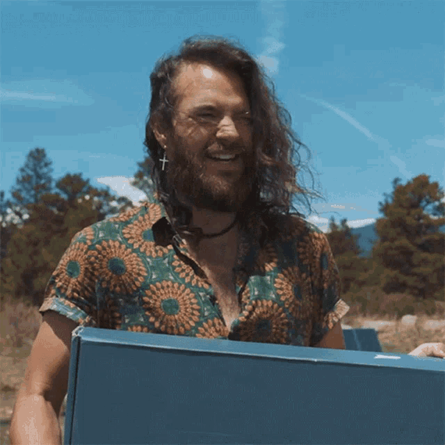 a man with long hair and a beard is holding a blue box and smiling