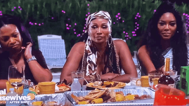 three women are sitting at a table with plates of food and a bottle of wine