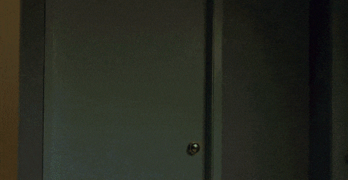 a person is standing in a dark room behind a blue door .
