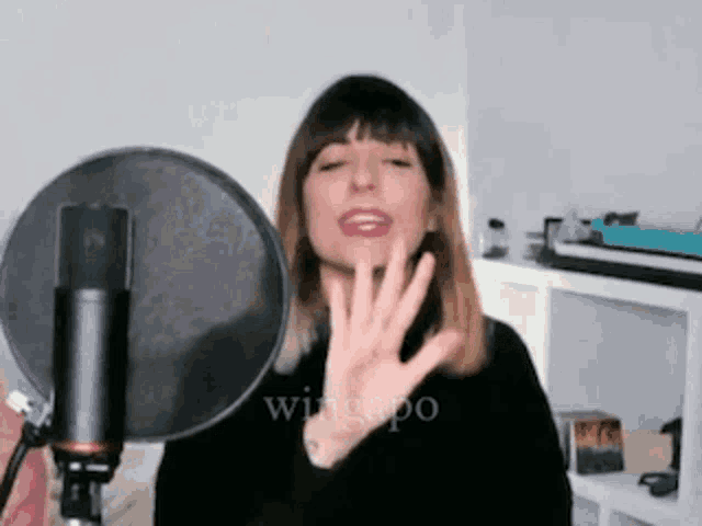 a woman is singing into a microphone and waving her hand in front of it .