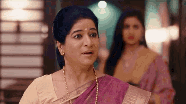 a woman in a purple saree is making a surprised face while another woman looks on .