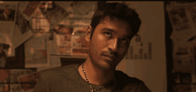 a man wearing a necklace looks at the camera in front of a wall with a graph on it
