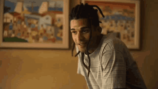 a young man with dreadlocks is standing in front of a painting .