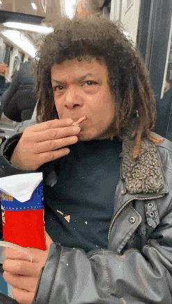 a man with dreadlocks is eating a french fry from a bag