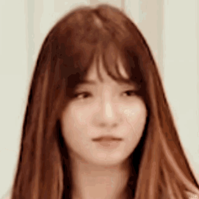 a close up of a woman with long brown hair and bangs making a funny face .