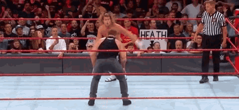 two men are wrestling in a wrestling ring with a referee and a sign that says heath on it .