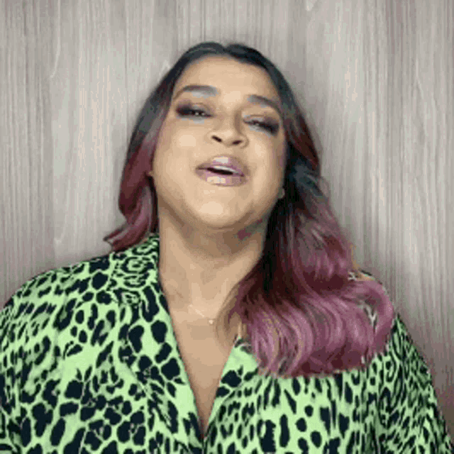a woman with purple hair is wearing a green leopard print jacket and making a funny face .