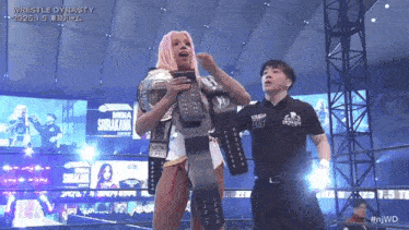 a woman with pink hair is holding a wrestling championship belt while standing next to a referee