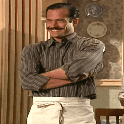 a man with a mustache and suspenders is standing with his arms crossed