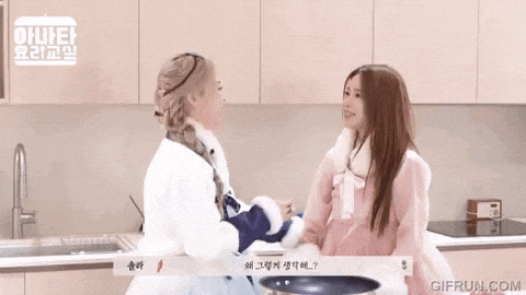 two women are standing next to each other in a kitchen and talking .