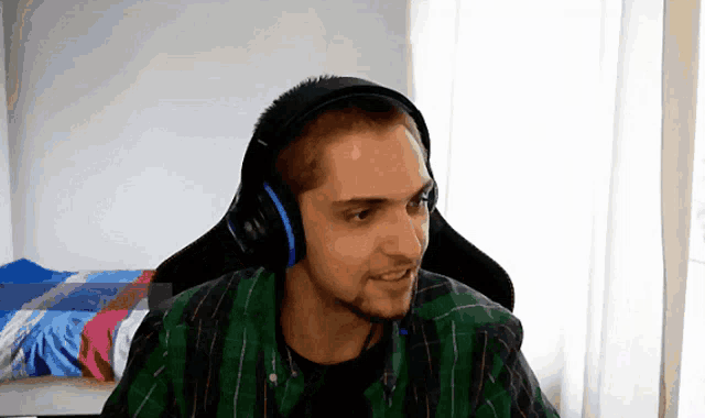 a man wearing headphones and a plaid shirt looks at the camera