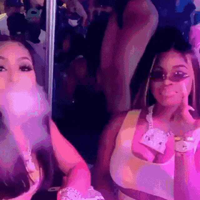 two women are blowing bubbles in front of a mirror while wearing sunglasses .