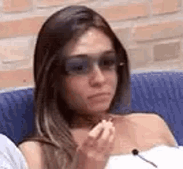 a woman wearing sunglasses is sitting on a blue couch eating a lollipop .