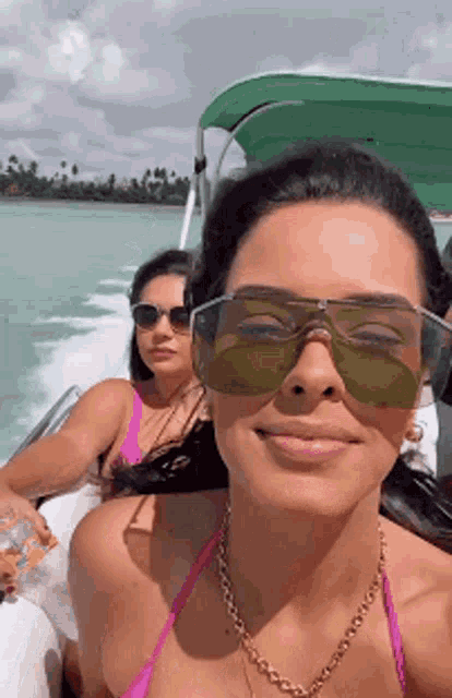 two women in bikinis and sunglasses are sitting on a boat in the ocean .
