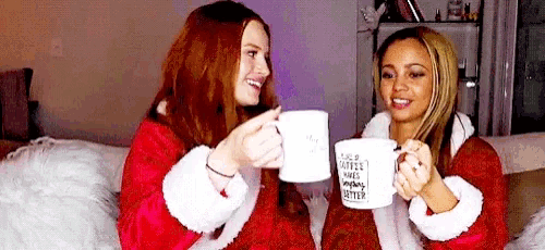 two women are sitting next to each other on a couch holding cups of coffee .