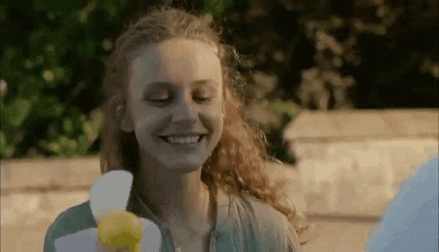 a woman is smiling while holding a lemon and a napkin in her hand .