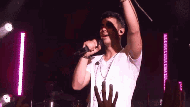 a man in a white shirt is singing into a microphone in front of a crowd