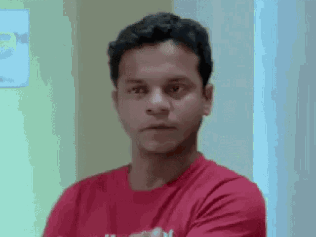 a man in a red t-shirt is standing with his arms crossed and looking at the camera .