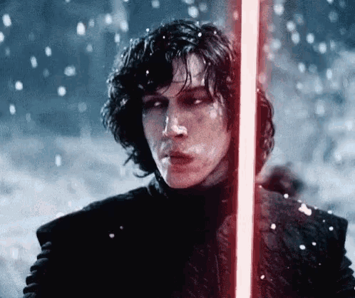 a man is holding a red lightsaber in the snow .