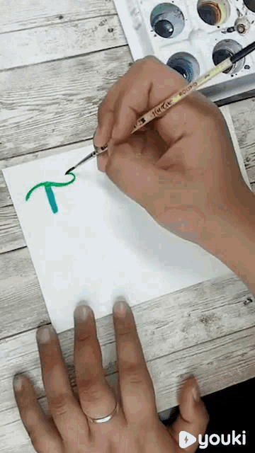 a person is painting the letter t on a piece of paper