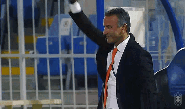 a man in a suit and orange tie is waving his hand