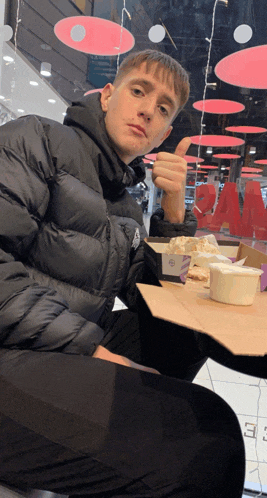a man in a black jacket is giving a thumbs up while sitting at a table