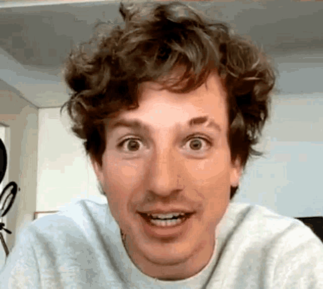 a man with curly hair is making a funny face while wearing a gray sweater .