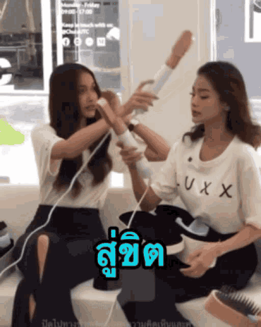 a woman wearing a luxx shirt holds a hair dryer over another woman 's head