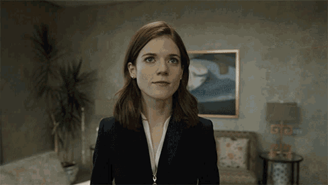 a woman in a suit stands in front of a painting on the wall