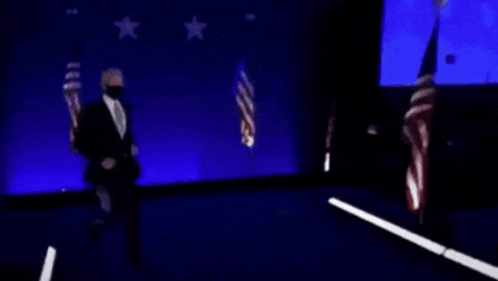 a man in a suit is dancing on a stage in front of american flags .