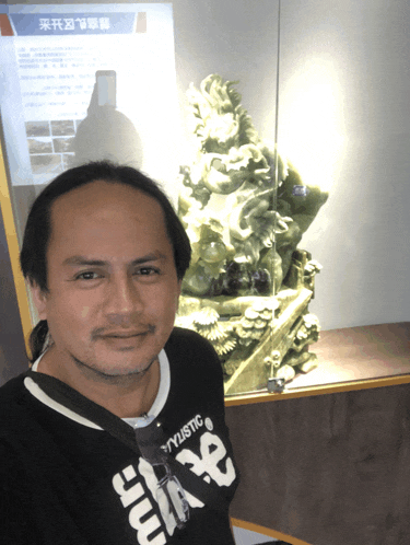 a man wearing a black shirt that says yylistic stands in front of a statue
