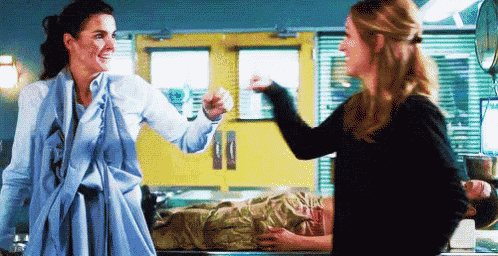two women are standing next to each other in a hospital room while a man is laying on a stretcher .