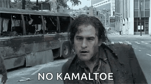 a man is walking down a street with a bus in the background and says `` no kamaltoe '' .