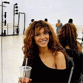 a woman with curly hair is smiling while holding a drink