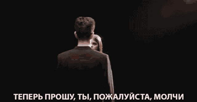 a man and a woman are standing next to each other in a dark room and looking at each other .