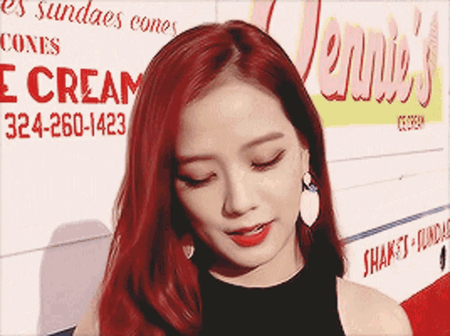 a woman with red hair stands in front of a sign that says jennie 's