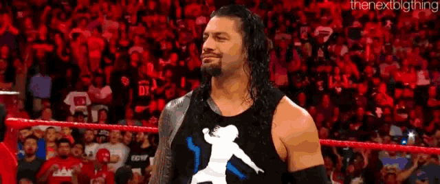 roman reigns is standing in a wrestling ring in front of a crowd of people .