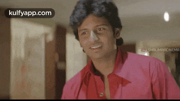 a man in a pink shirt is smiling in front of a screen that says kulfapp.com