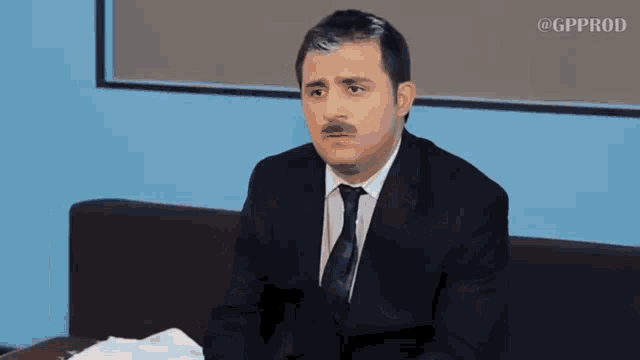 a man in a suit and tie is sitting on a couch looking at something .