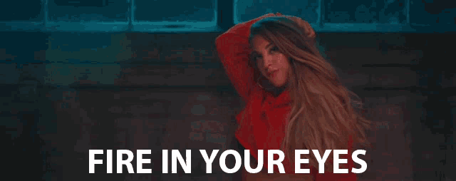 a woman in a red hoodie is standing in front of a brick wall with the words `` fire in your eyes '' .