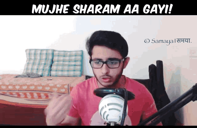 a man wearing glasses stands in front of a microphone with the words mujhe sharam aa gayi written below him