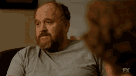 a man with a beard and bald head is sitting on a couch talking to another man .